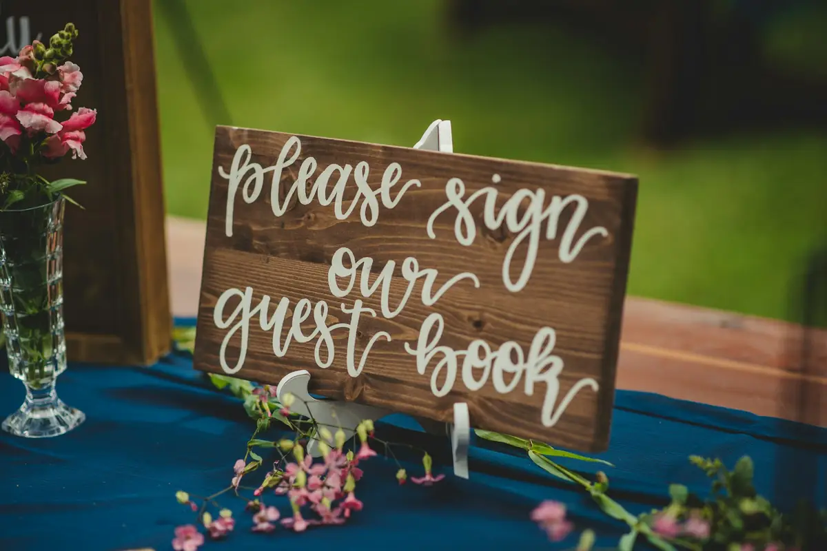 A wooden sign saying please sign our guest book on a wedding table